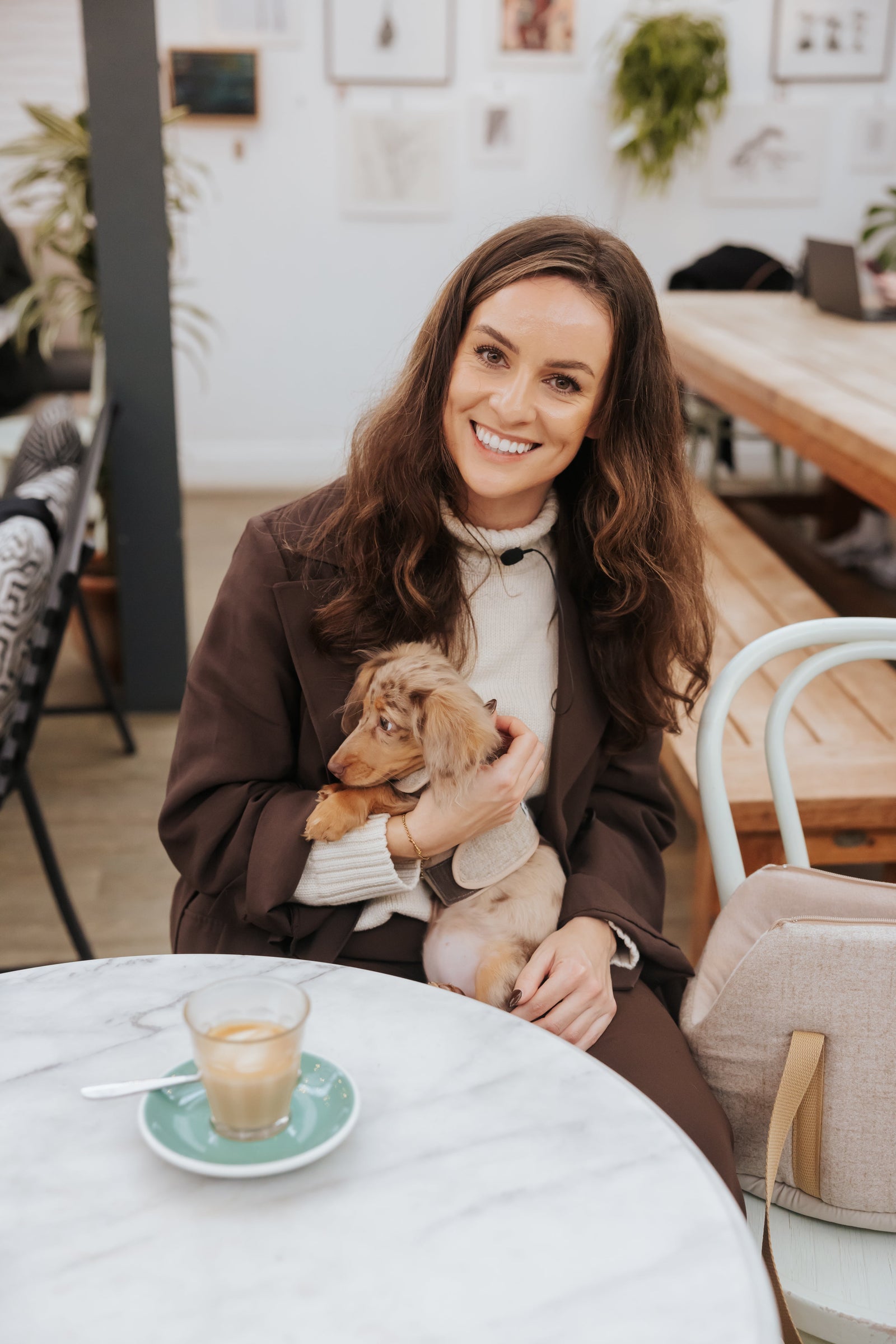 Woman holding a small dog in a cafe setting with a cup of coffee on the table.