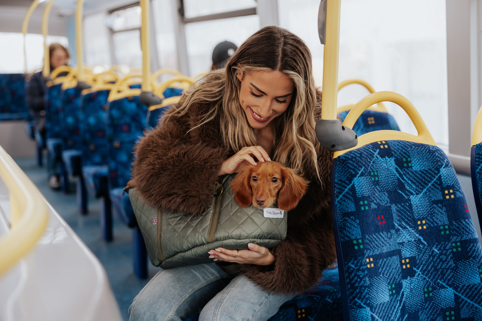 Woman holding a small dog in a pet carrier on a bus